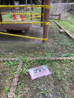 立ち入り禁止の黄色いテープで囲まれた場所と、その近くに落ちている防犯カメラ設置中の看板の写真