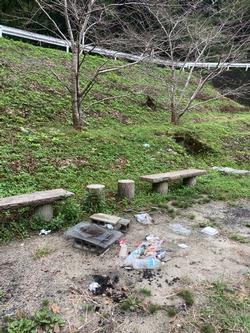 緑の草が生い茂る斜面の下にベンチとゴミが散乱している光景