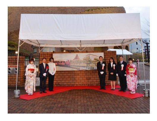 銘板のデザインの前で集合写真