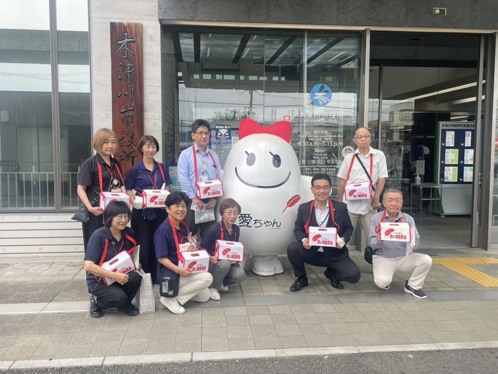 木津川市役所前で赤い羽根共同募金のマスコットキャラクターとスタッフと一緒に集合写真