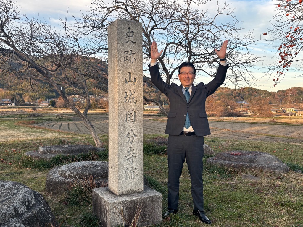 史跡山城国分寺跡の右横で、両手を上げてポーズをとる市長の写真