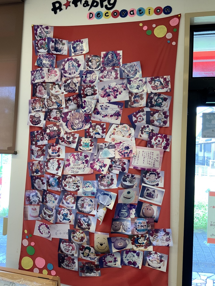 沢山の「似顔絵デコレーションケーキ」の写真を貼り出したボード